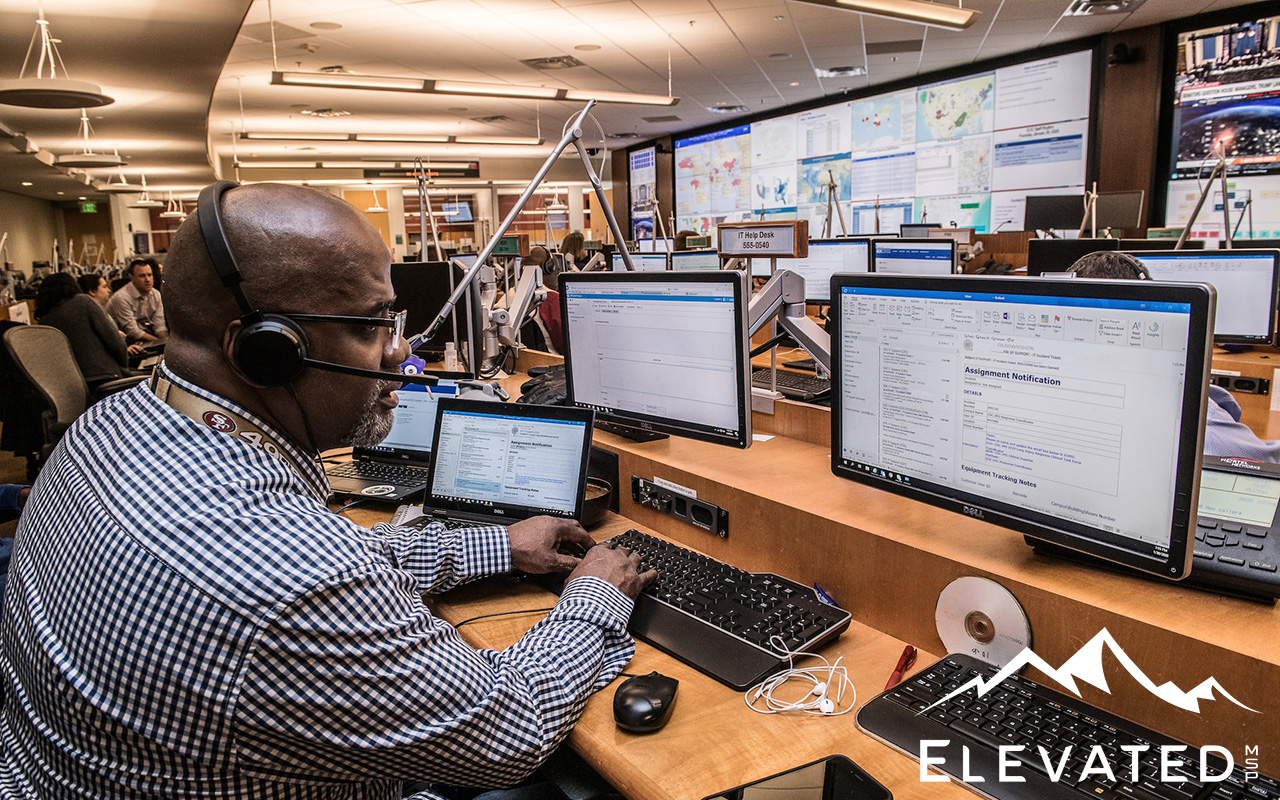 Bald black man sitting in front of a bank of computers.