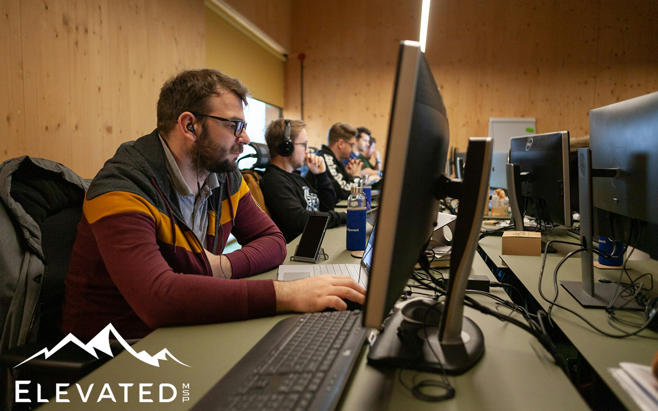 Group of men working at a long desk covered with keyboards and computer monitors.